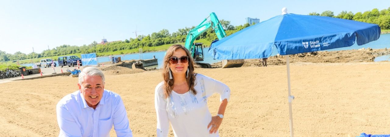 Készülő homokos strand háttérben munkagépekkel, előtérben egy férfi és egy nő